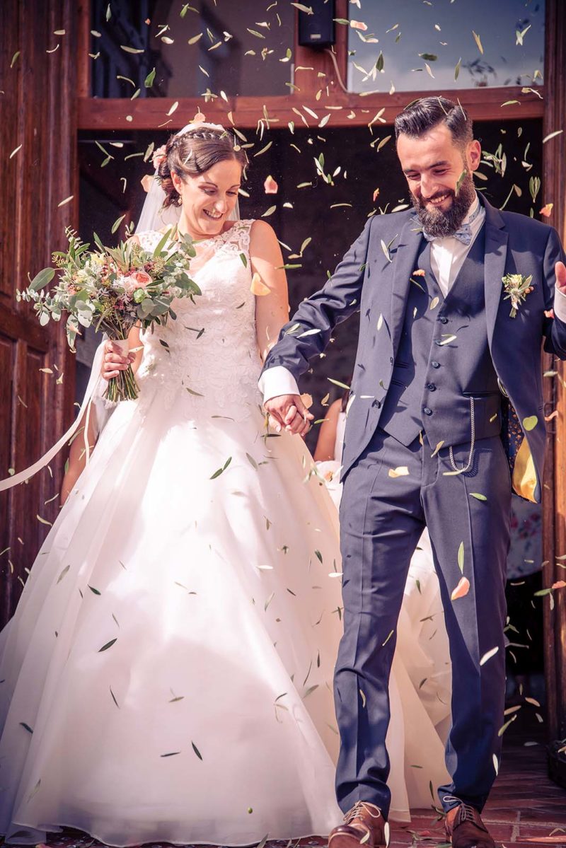 couple de mariés sortant de l'église sous une pluie de feuilles d'olivier