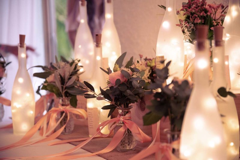 décoration de mariage avec des bouteilles en verre illuminées et des petits vases avec des fleurs