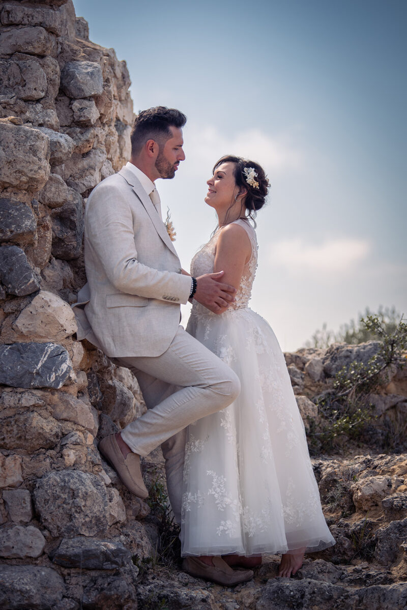 photo de deux mariés appuyés sur un mur de pierre