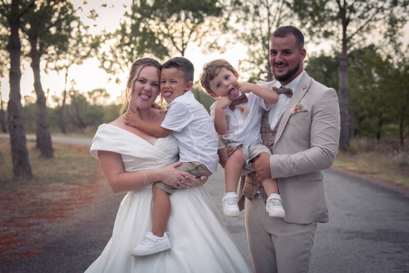 photo d'un couple de jeunes mariés avec leurs enfants dans les bras sur un chemin au coucher de soleil