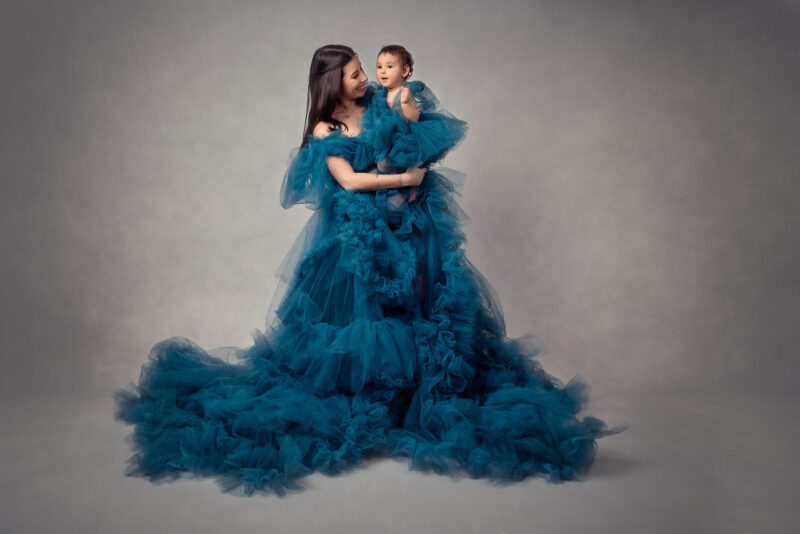femme brune avec des cheveux longs habillée d'une robe en tulle bleue et tenant son enfant habillée pareil qu'elle