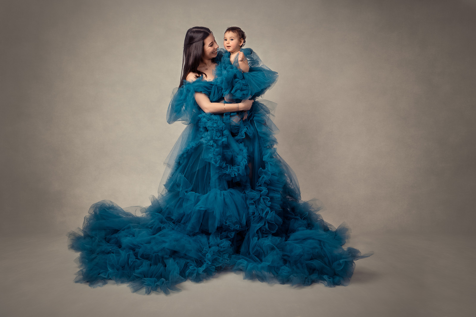 femme brune habillée d'une robe en tulle bleu et tenant son enfant qui est habillée pareil qu'elle
