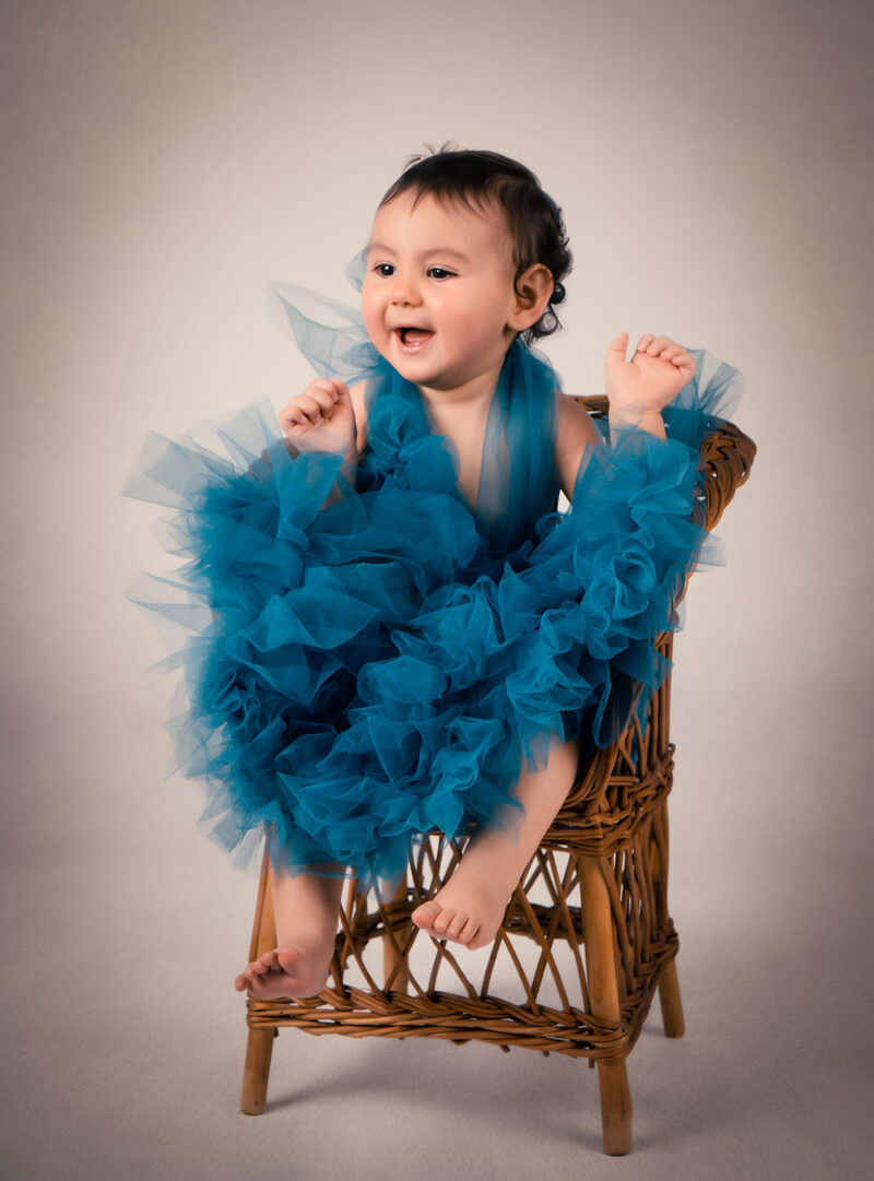 jeune enfant vêtue d'une robe bleue en tulle assise sur une petit chaise en osier