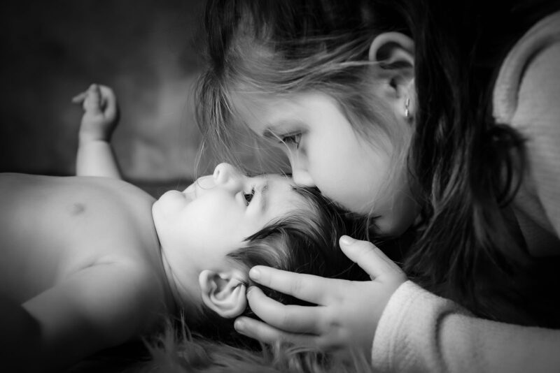 photo noir et blanc d'une grande sœur embrassant son petit frère sur le front