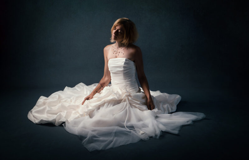 photo studio femme blonde en robe de mariée en position assise les yeux fermés