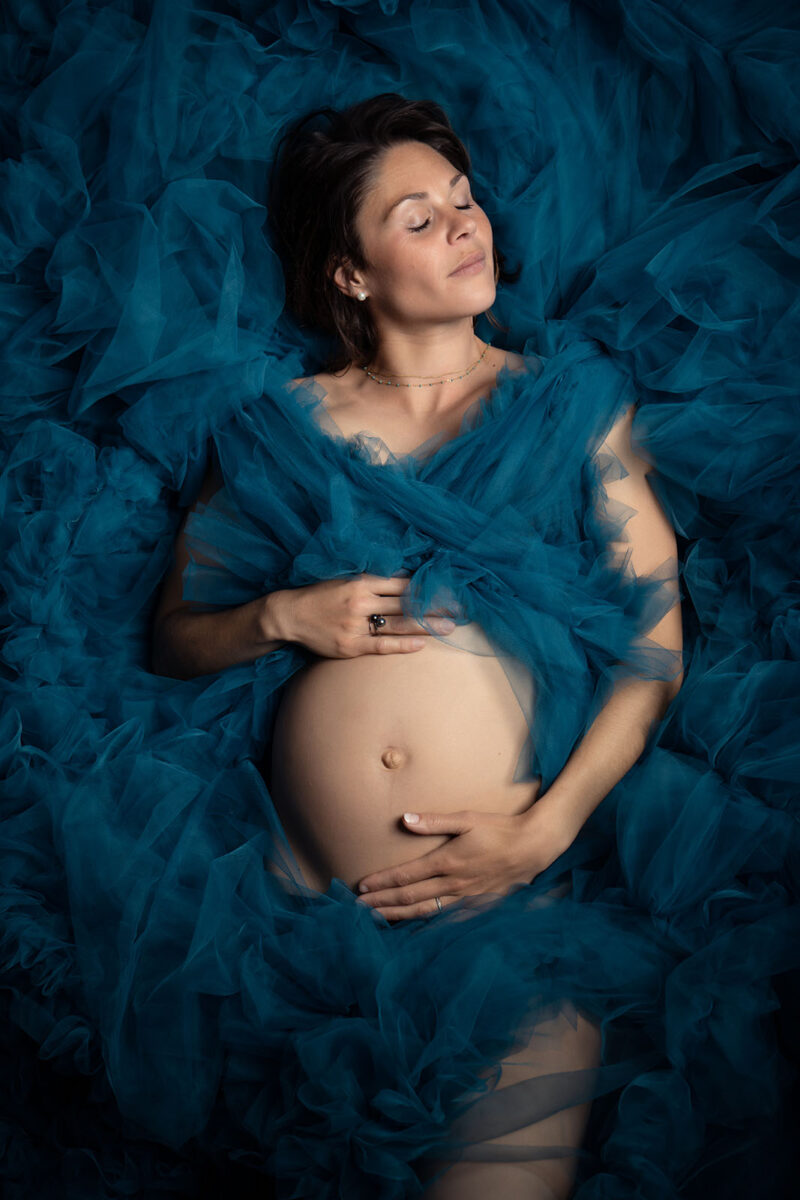 portrait d'une femme enceinte allongée au sol prise du dessus entourée de tulle de couleur bleu
