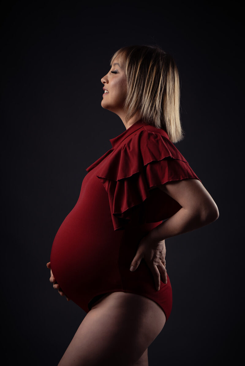 portrait de profil d'une femme enceinte blonde avec un body rouge et des manches courtes à frourfrou