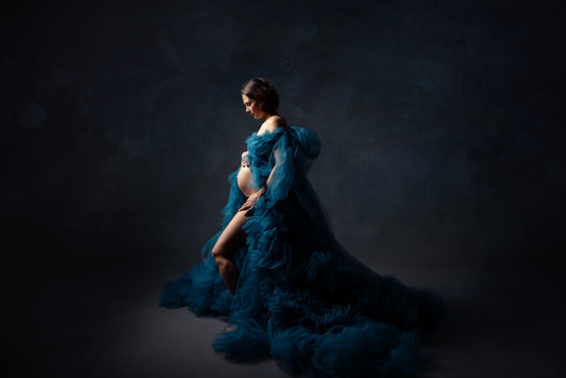 portrait en studio d'une femme enceinte de profil portant une longue robe de tulle volumineuse de couleur bleue