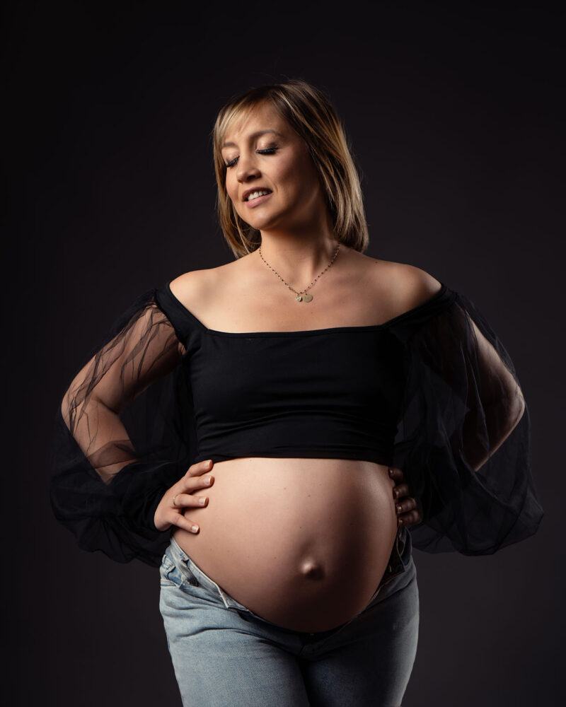 Portrait d'une femme enceinte portant un crop top noir avec des manches en tulle et en jean ouvert