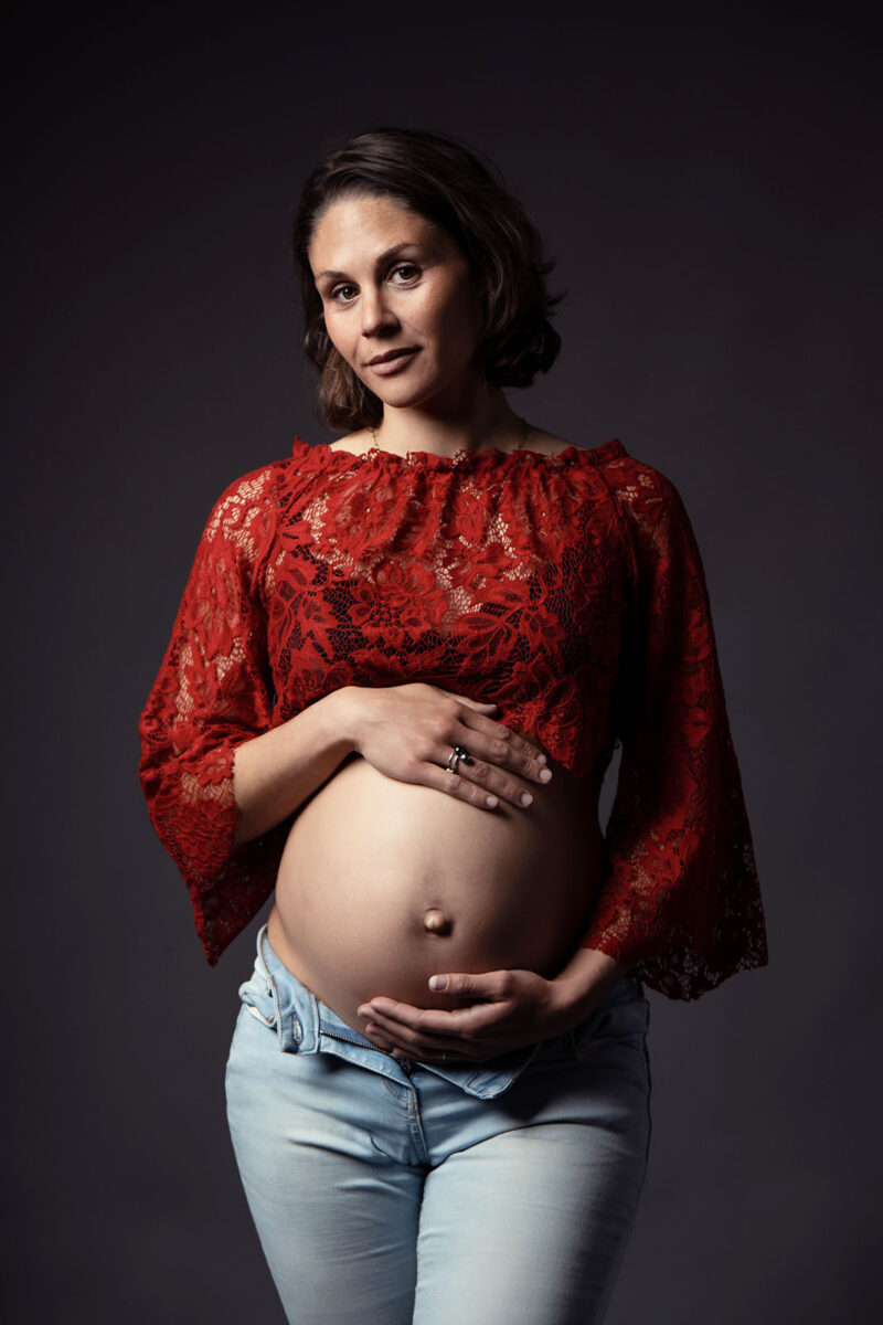 portrait d'une femme enceinte de face avec un boléro rouge en dentelle et un jean