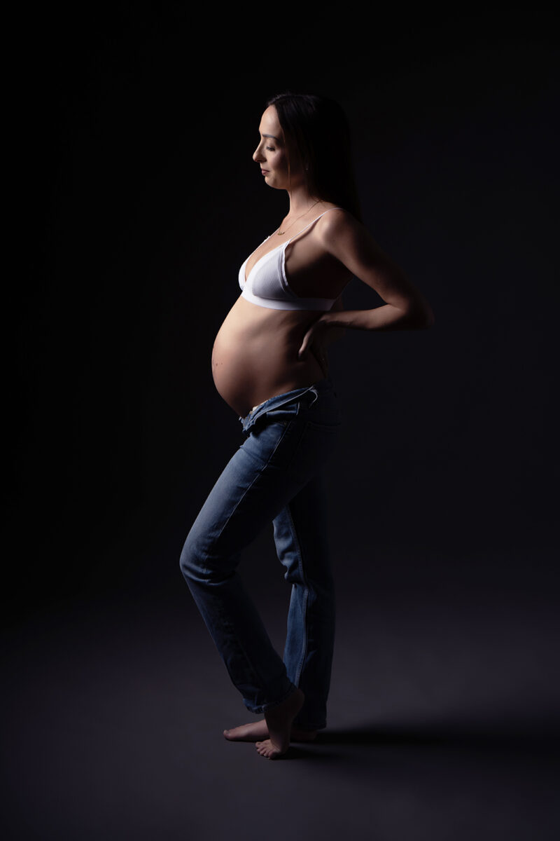 portrait de profil d'une femme enceinte habillée en jean bleu et soutien gorge blanc