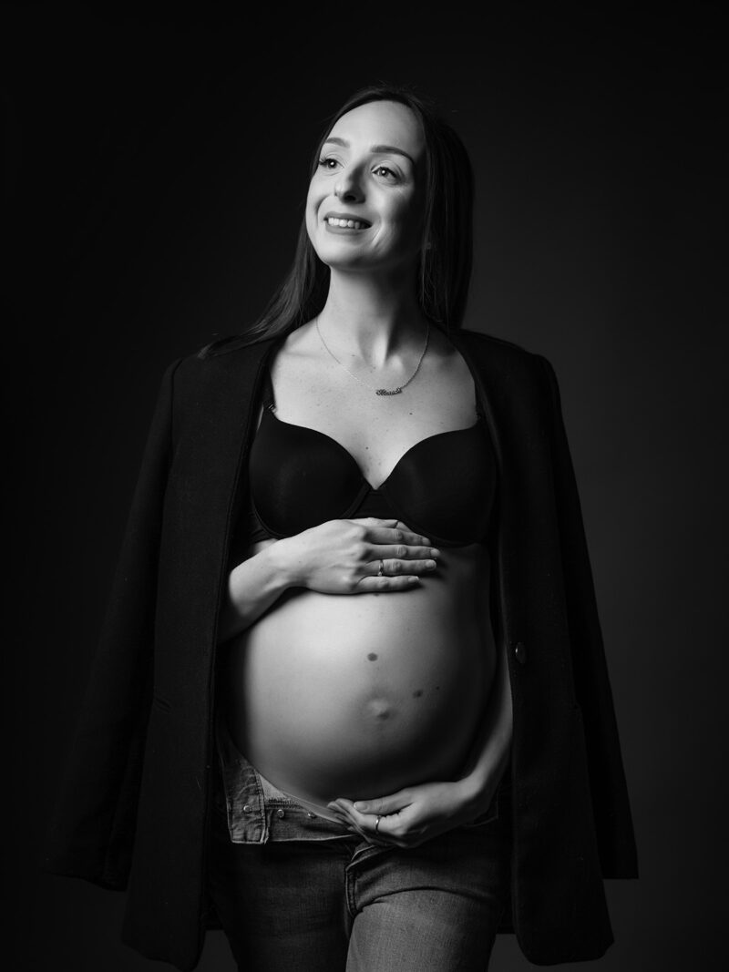 portrait noir et blanc d'une femme enceinte en soutien gorge noir et veste de blazer qu'elle a posé sur ses épaules