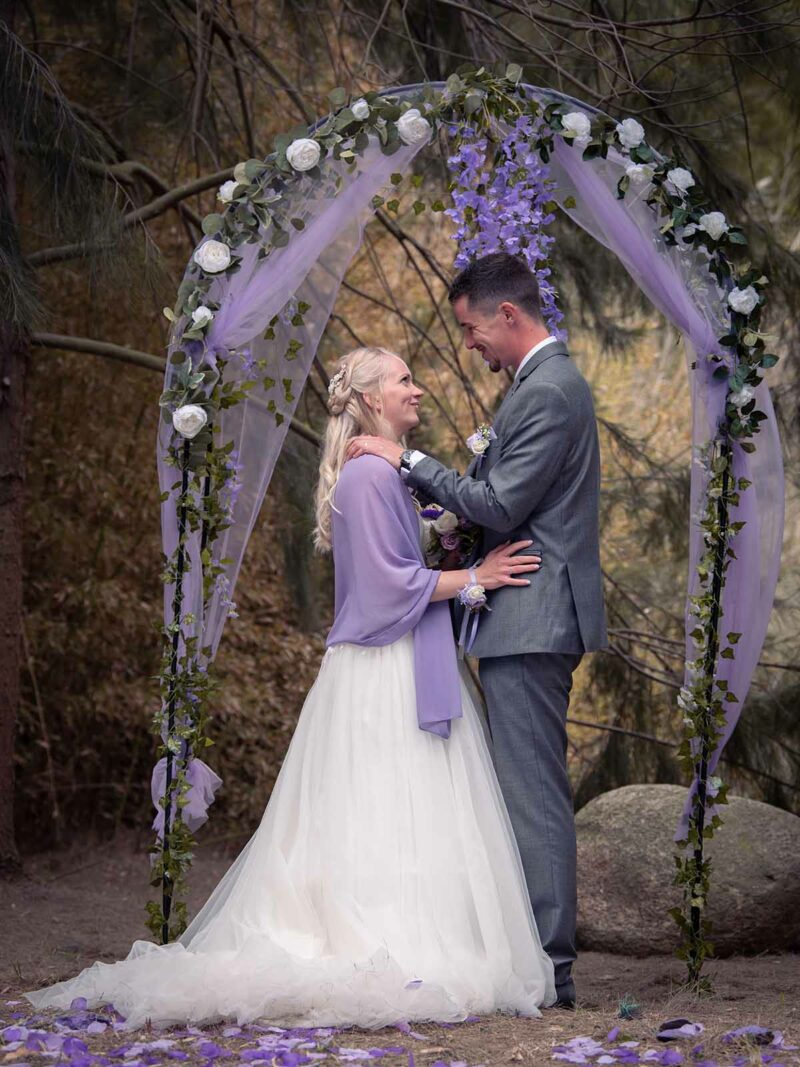 photo d'un couple de marié sous une arche habillée de tulle couleur Lilas