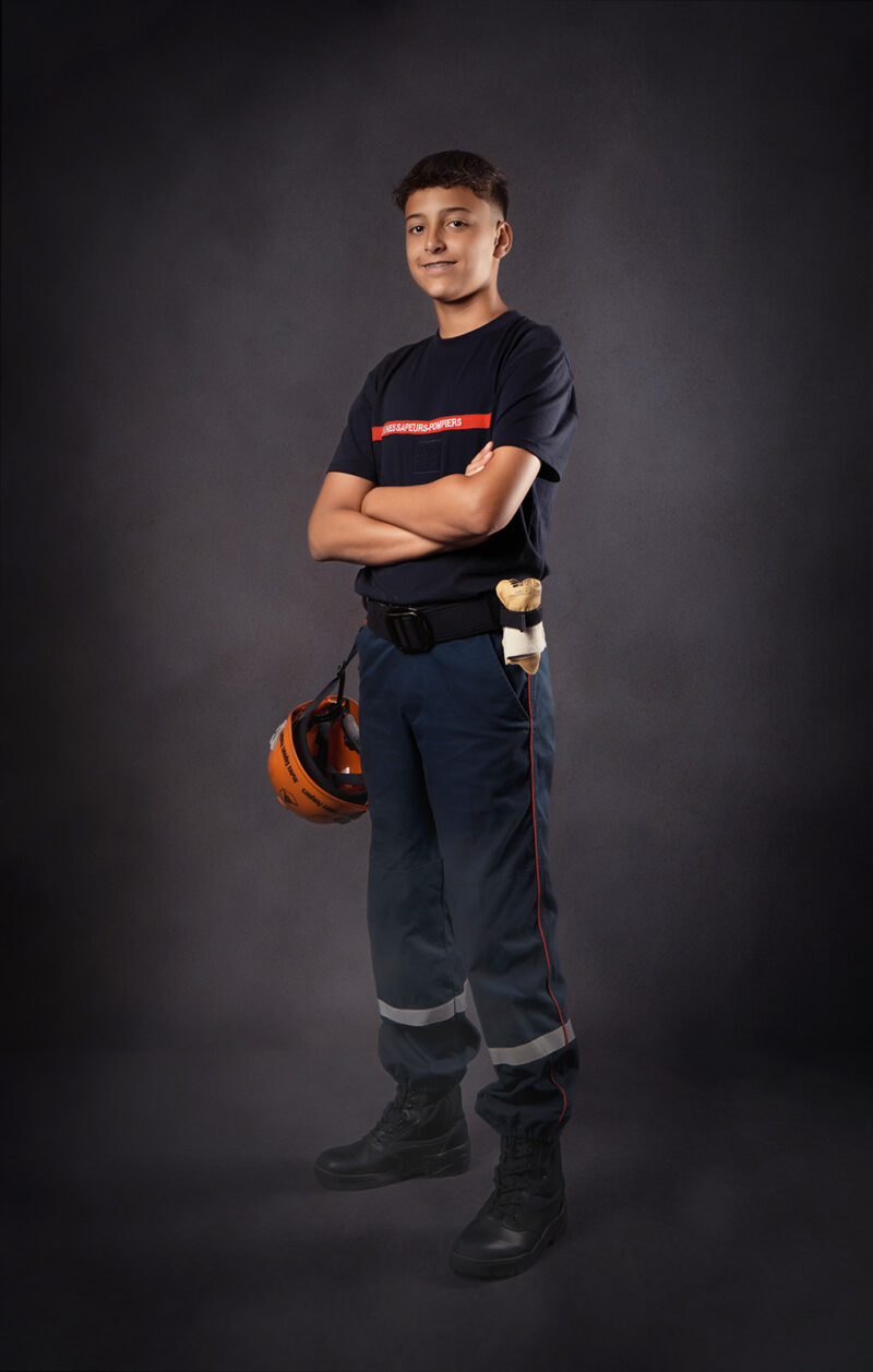 photo studio d'un jeune homme habillé en tenue de sapeur pompier se tenant debout les bras croisés