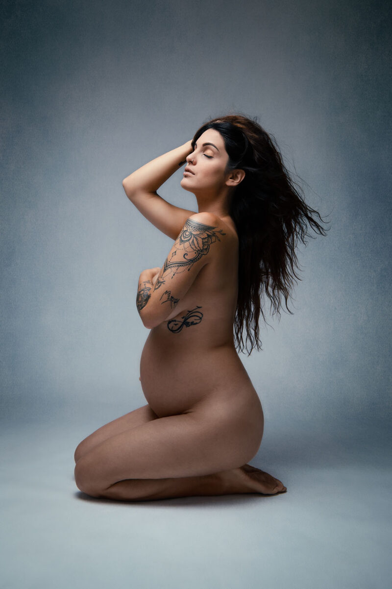 portrait studio d'une femme enceinte nue tatouée assise au sol