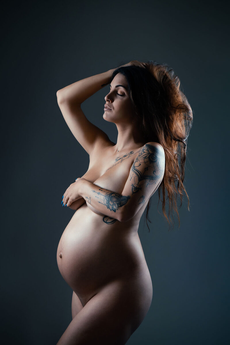 Clair obscur en couleur d'une femme enceinte nue tatouée