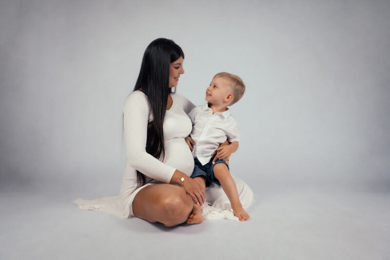 photo studio d'une femme enceinte assise qui porte son enfant sur les genoux