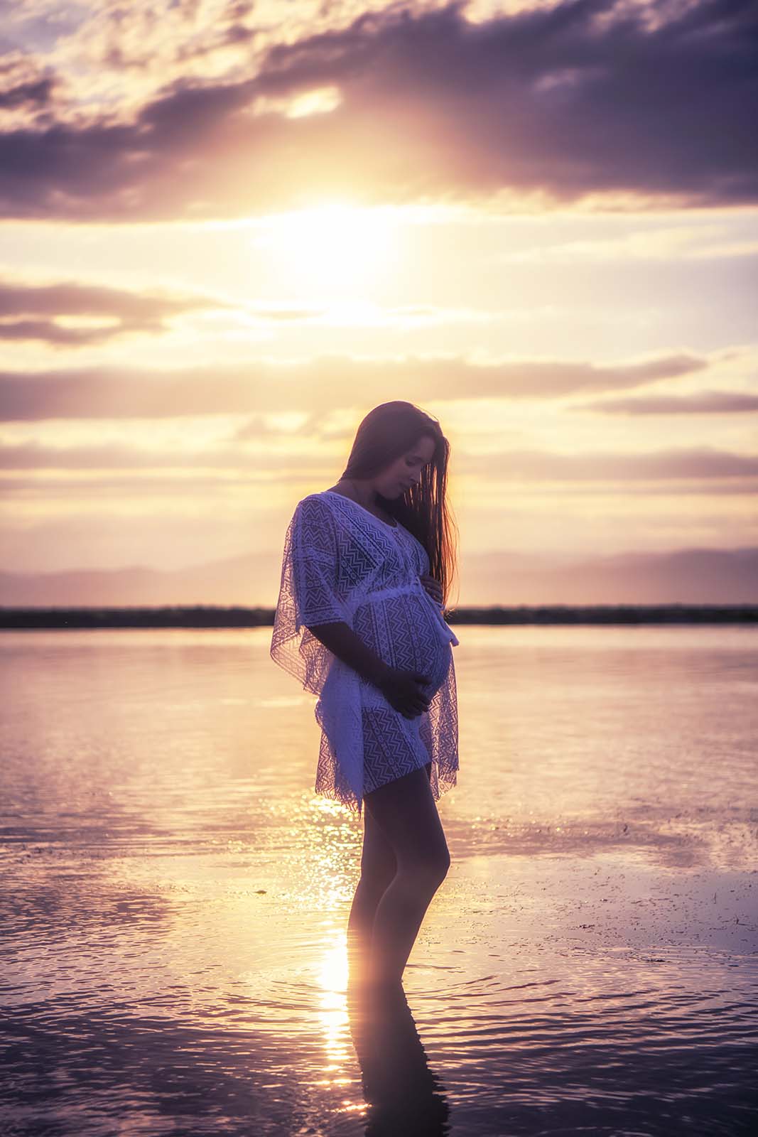 Photo d'une femme enceinte les pieds dans l'eau au coucher de soleil