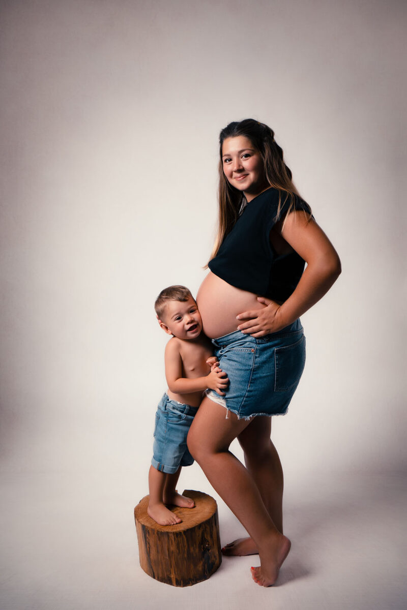 photo studio d'une femme enceinte avec son enfant qui a la tête posé sur le ventre de la maman