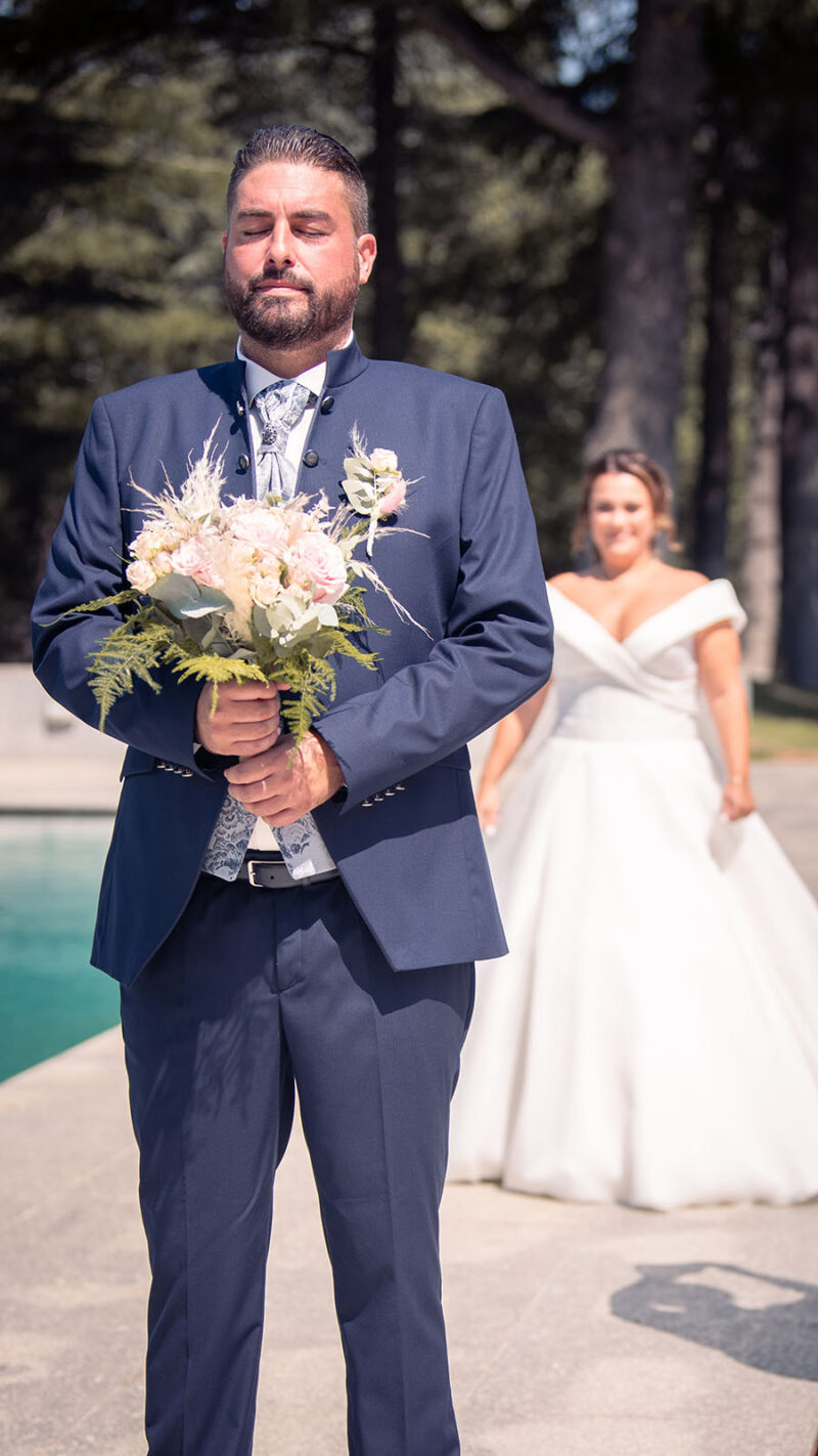 photo du marié tenant le bouquet , la mariée arrive derrière lui