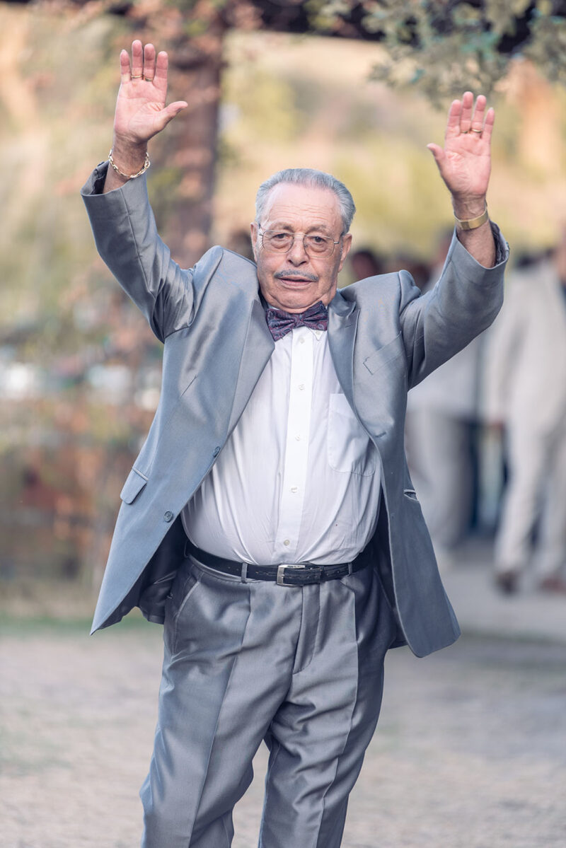 photo d'un vieux monsieur habillé en costume gris levant les bras