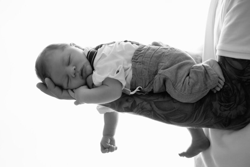 photo noir et blanc en contre jour d'un bébé posé sur le bras de son papa