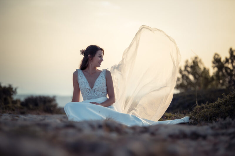 mariée assise dans un chemin de pierre regardant son voile voler