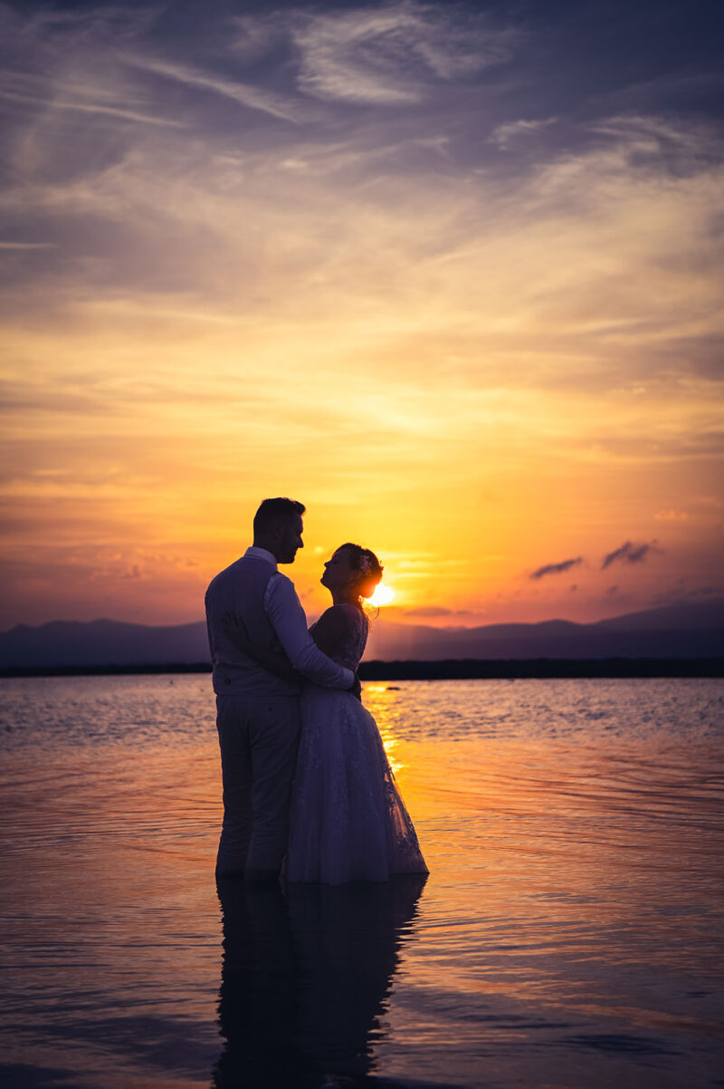 couple de mariés le pieds dans l'eau au coucher de soleil se tenant dans les bras