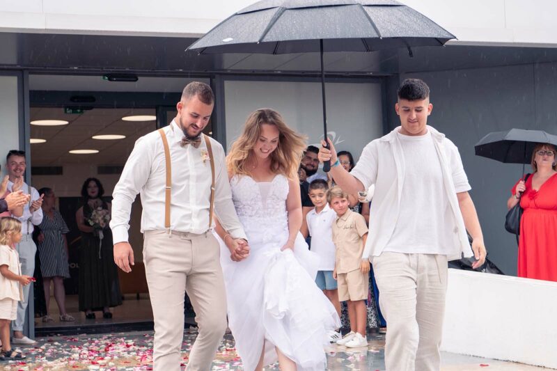 couple de mariés sortant de la mairie sous un parapluie