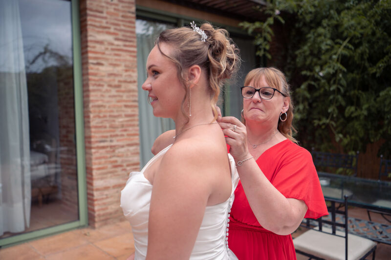 photo de la maman d'une mariée en train de lui accrocher son collier