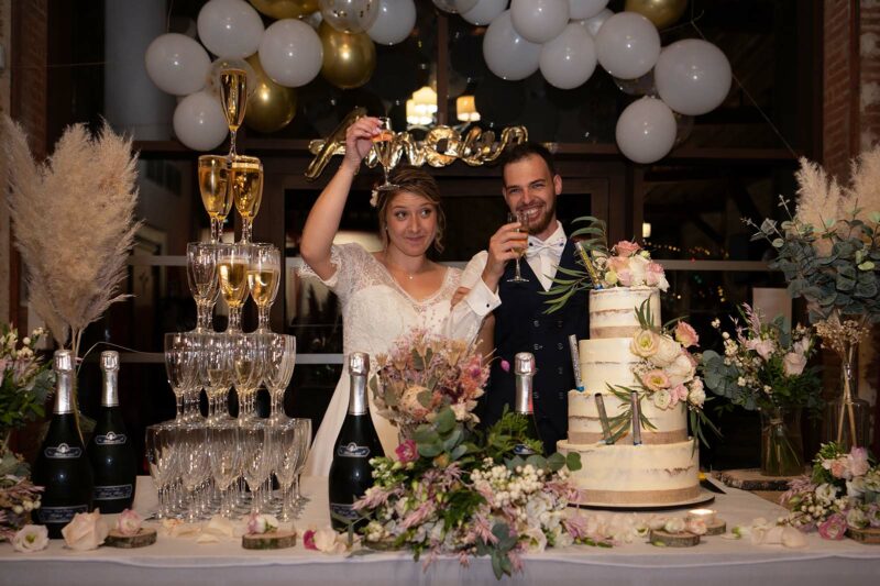 photo de mariés levant une couple de champagne derrière leur gâteau