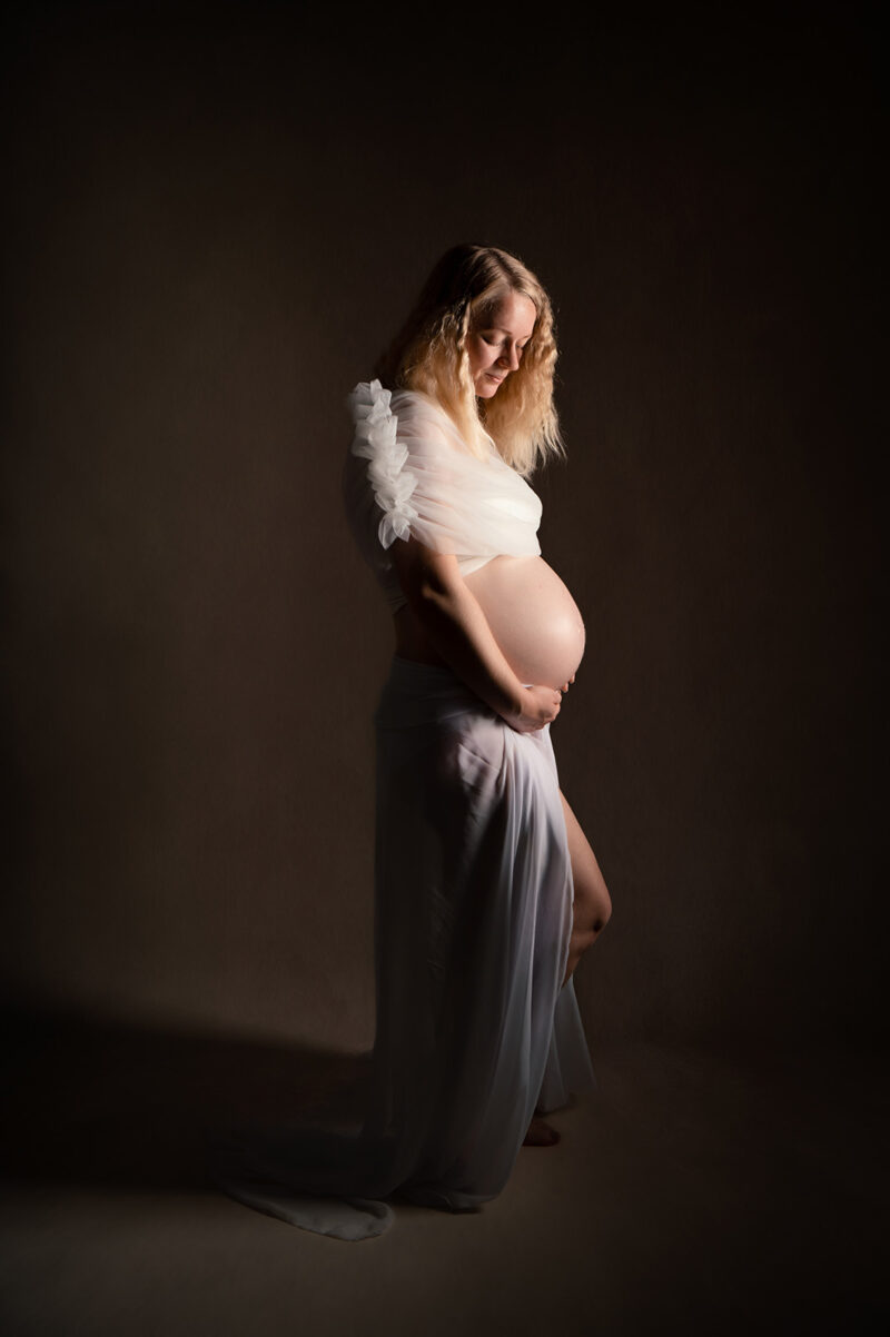 photo studio d'une femme enceint habillée d'une tenue blanche laissant dévoiler son ventre