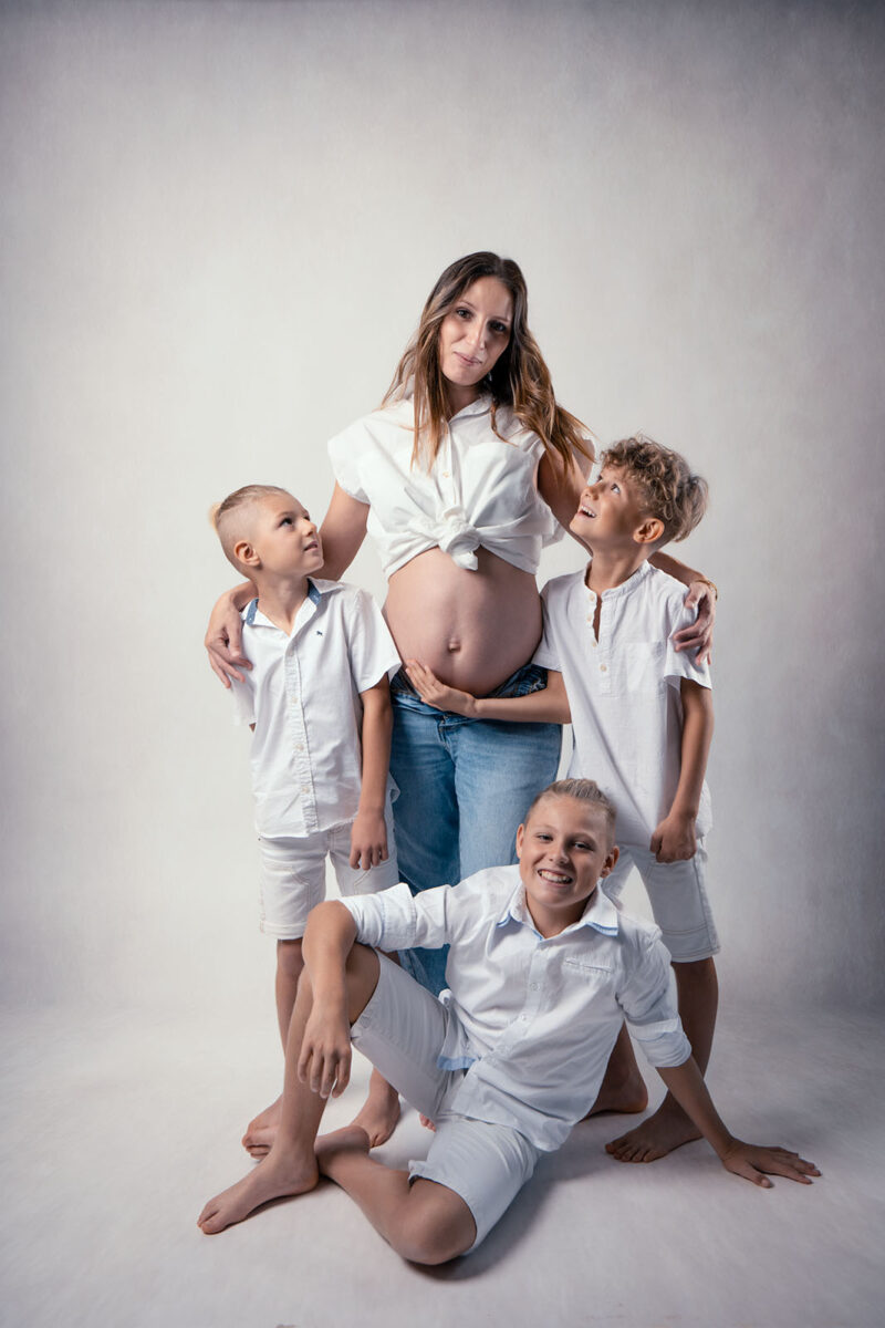 photo studio sur fond clair d'une femme enceinte avec trois jeunes garçons