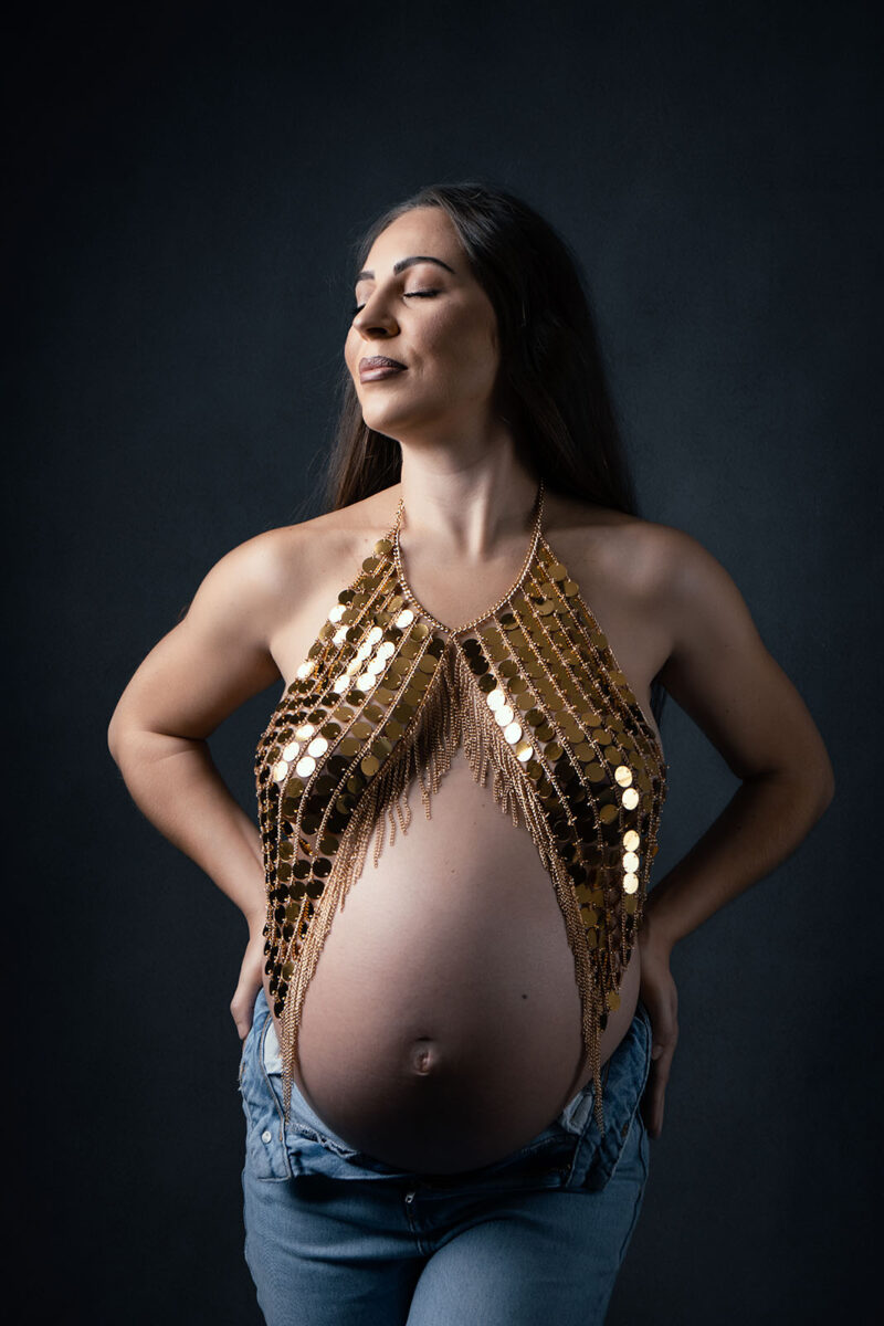 Photo studio d'une femme enceinte portant un bijou de corps doré
