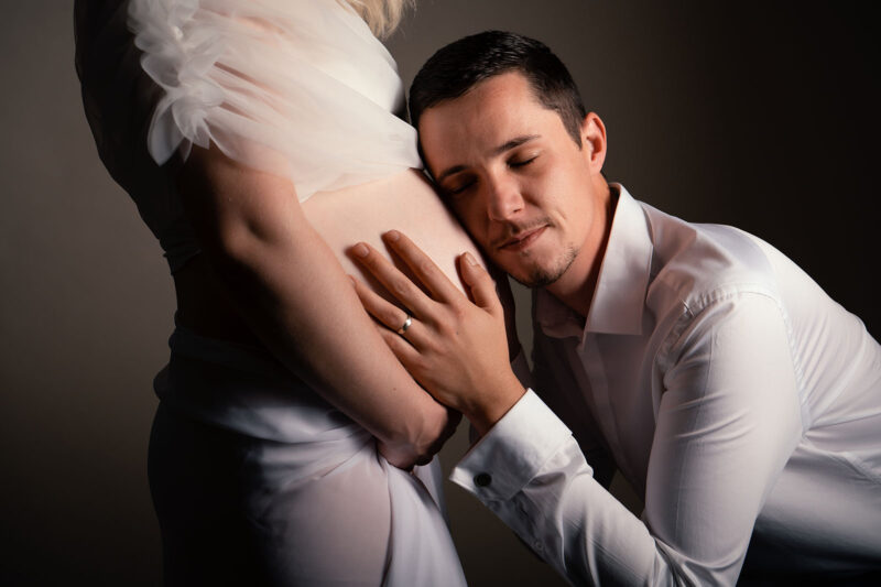 photo studio d'un homme posant la tête en fermant les yeux sur le ventre de sa femme