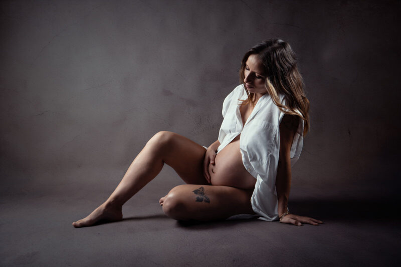Photo studio d'une femme enceinte assise au sol avec une main sur le ventre