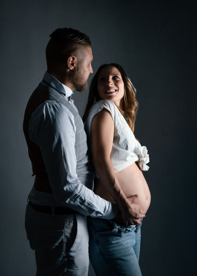 photo studio d'un couple en clair obscur, la femme est enceinte et l'homme habillé en costume