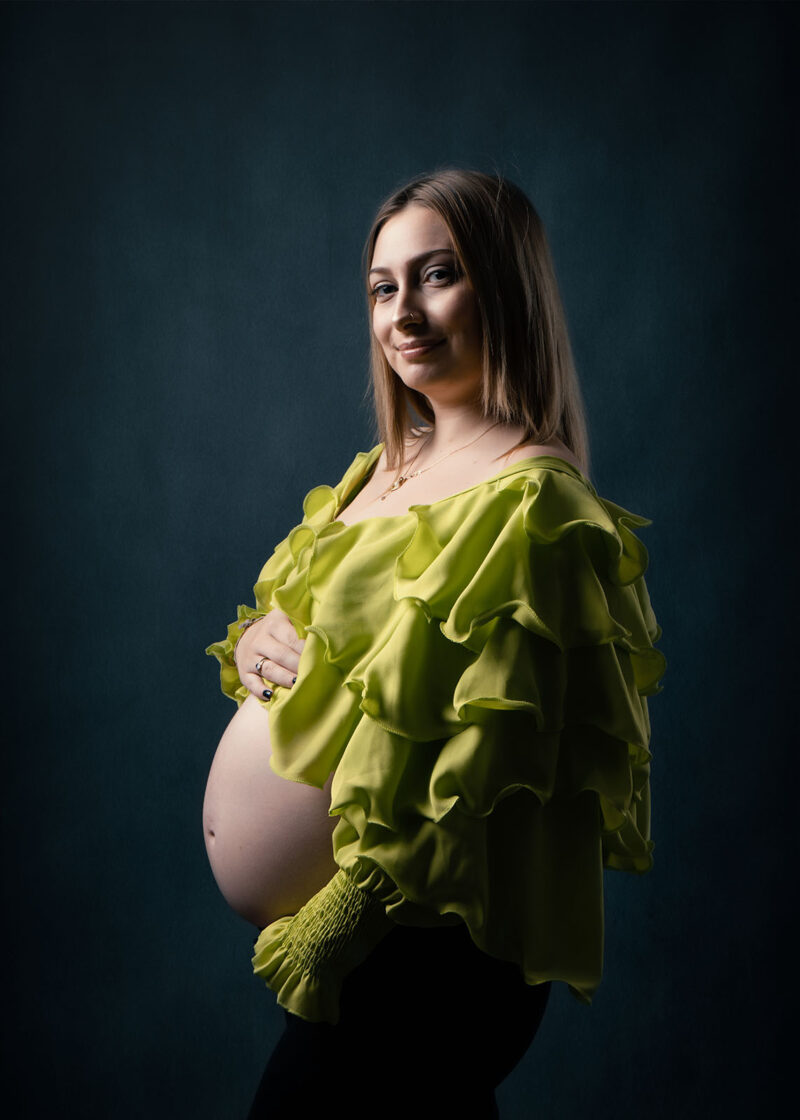 photo prise en studio d'une femme enceinte portant un haut vert avec des volants