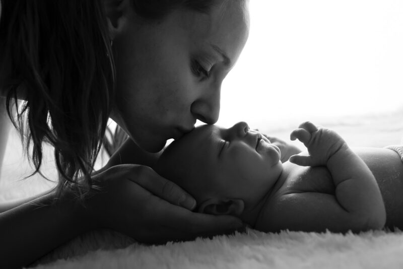 photo en contre jour d'un maman embrassant son bébé sur le front