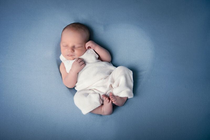 photo d'un nouveau né prise du dessus où on voit le bébé allongé sur le dos dans un contenant en forme de cœur recouvert d'un tissu bleu