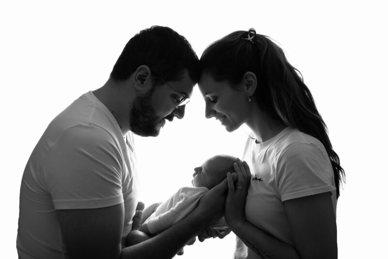 photo en contre jour de deux parents pris de profil tenant un bébé dans leur bras