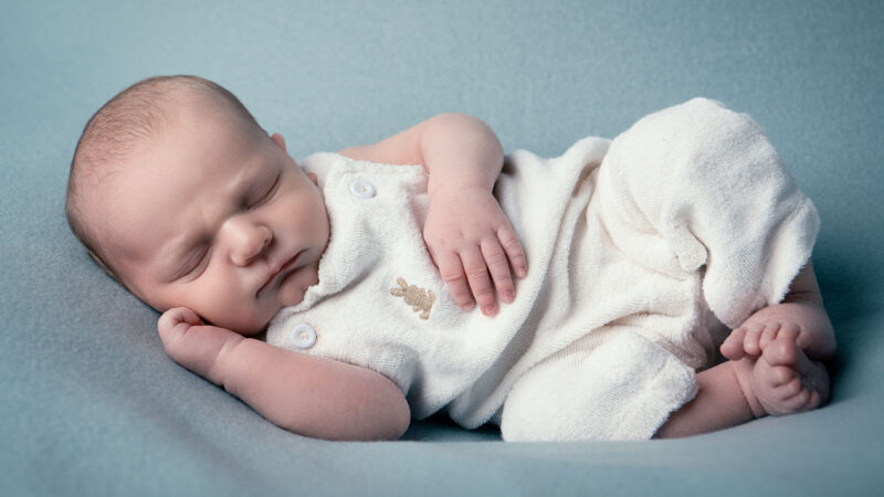 photographie d'un nouveau né allongé sur le coté sur un tissu bleu