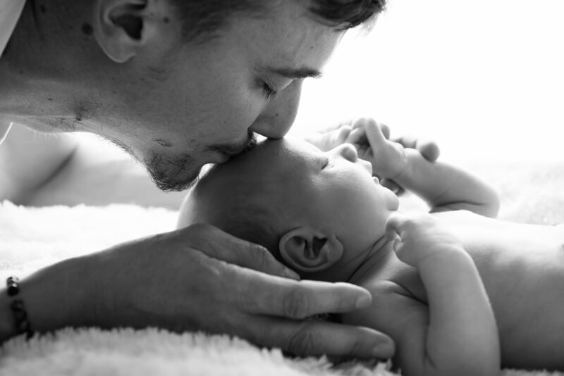 photographie en contre jour d'un papa embrassant son bébé sur le front