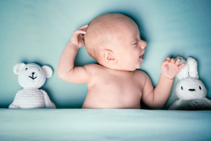 Photographie d'un nouveau-né sous une couverture bleue clair entourée de deux petits nounours