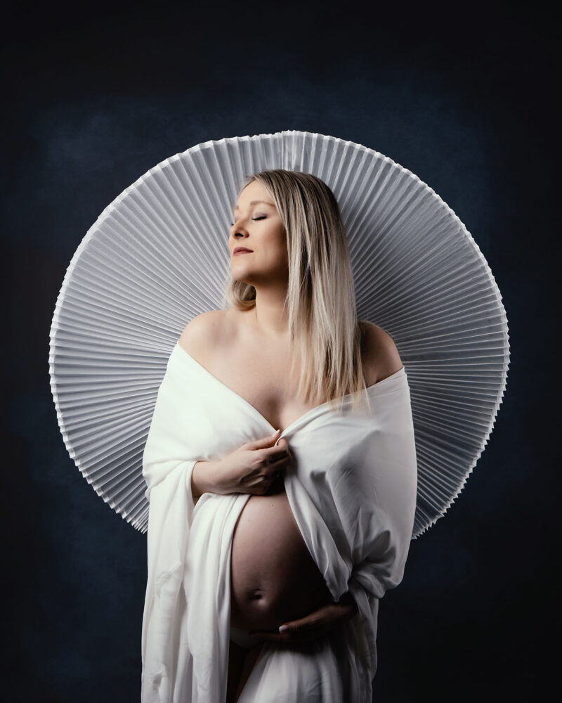 photo studio d'une femme blonde enceinte avec un tissu plissé derrière elle