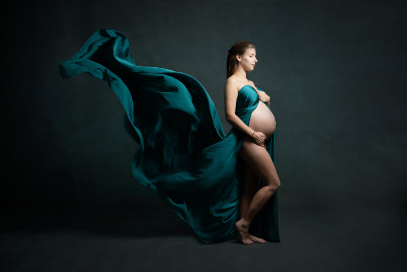 photo studio d'une femme enceinte portant un voile vert volant, la photo est prise de profil