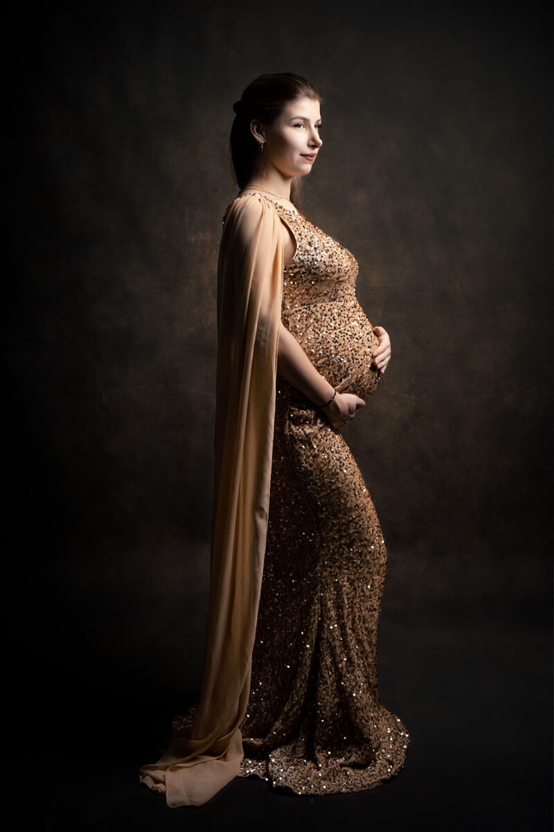 photo studio d'une femme enceinte portant une robe sirène de couleur champagne sur fond marron