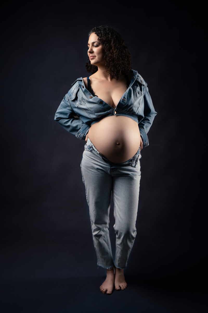 photo studio d'une femme enceinte se tenant debout et étant habillée tout en jean
