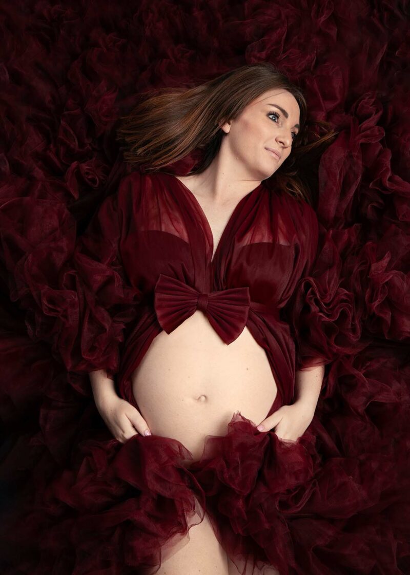 photo studio d'une femme enceinte allongée au sol et portant une grosse robe en tulle rouge