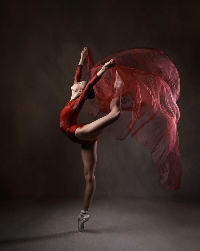 photo studio d'une danseuse classique faisant un arabesque avec un voile rouge
